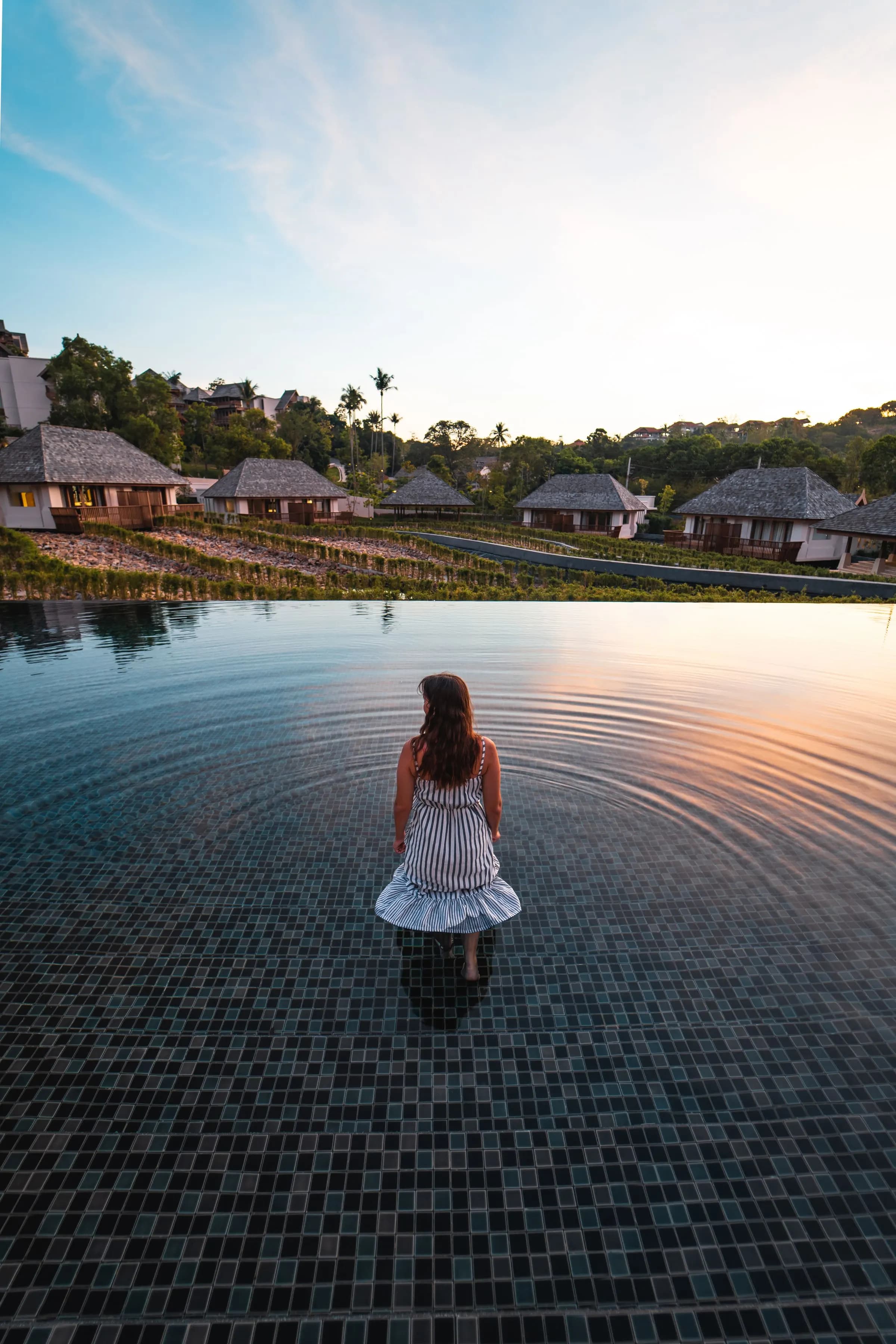 Guest standing in an infinity pool at dusk with villas behind